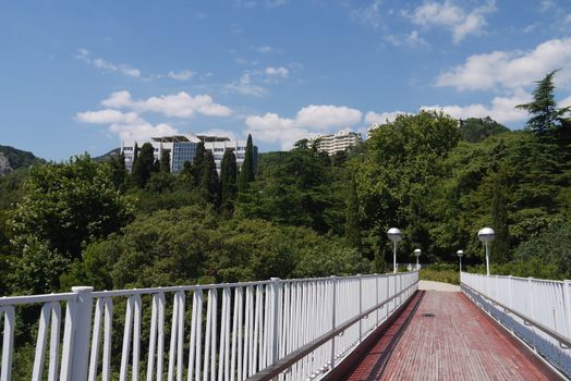 A small bridge with white railings leading to beautiful spa buildings in the shade of green mountain trees