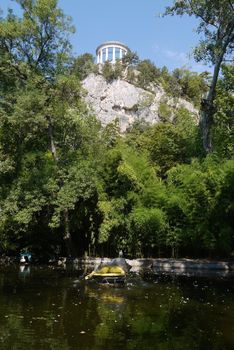 Green lake with a decorative fountain on the background of a high rocky mountain with a white observation platform