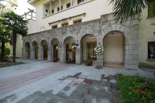 Beautiful building of a sanatorium complex with wide gray stobas, palms and decorative hanging flowers