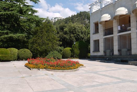 a flower bed on a background of a building, round decorative bushes and firs