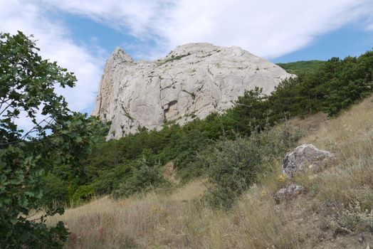 A stone rock with a spike on the top is clothed on a hill on a blue sky background