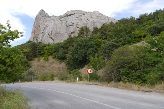 A steep road turn on a background of green vegetation and a high rocky mountain