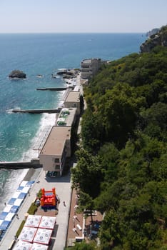 A large embankment with hulls for tourists, restaurants, children's playgrounds and piers on the background of mountains and the blue sea