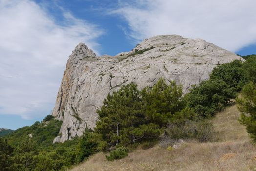 Green slope against the background of a high massive rocky mountain and blue sky