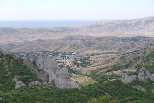 The road running between the green slopes of the mountains to a small village lying in the valley. In an environment completely empty without vegetation and trees.