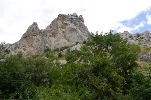 Rocky steep mountain peak against a background of low deciduous trees