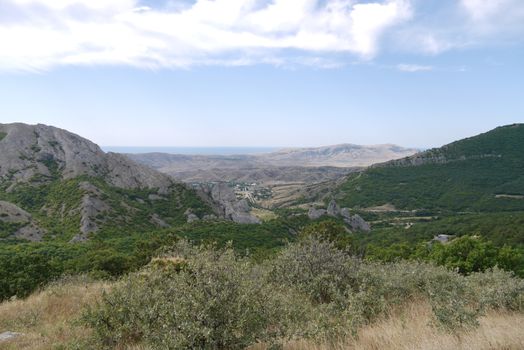 A landscape of mountainous terrain with mountain peaks and valleys covered with green forest and completely bare without a single tree.