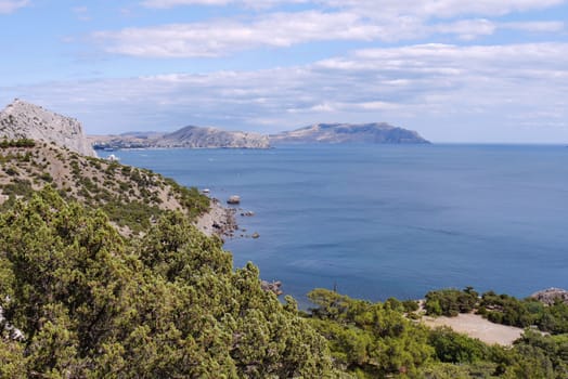 Magnificent landscape from the green mountain slope to the watery surface of the blue sea with standing rocks in the distance.