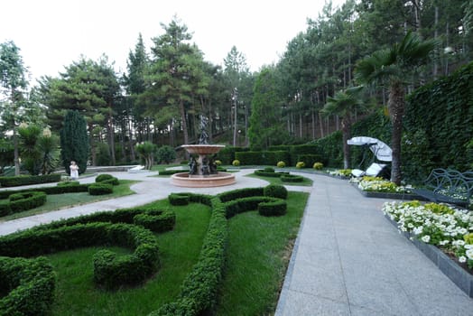 Magnificent design in a park with beautiful green lawns benches for rest among bright colors and a fountain with sculptures.