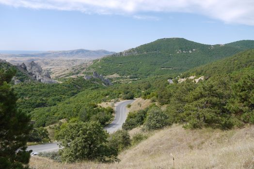 Rocky mountain peaks in the neighborhood with green overgrown forests and the road running between them