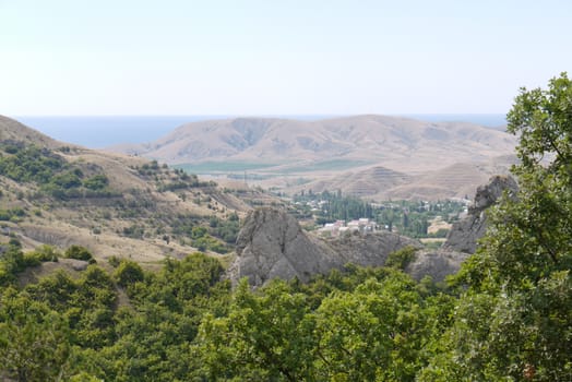 Stony ledges among the lush foliage of trees with the houses of a small village lying below in the valley with bare slopes.