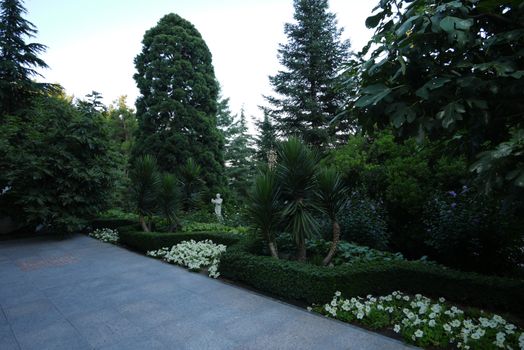Garden with trees, palm trees, flowers and bushes in which stands a white statue of a man