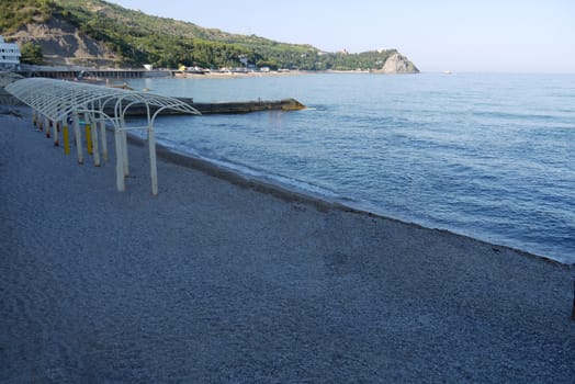 The deserted shore of the beach with a long pier overlooking the sea and a beautiful view of the slopes of the coast opposite with a green scenic nature.