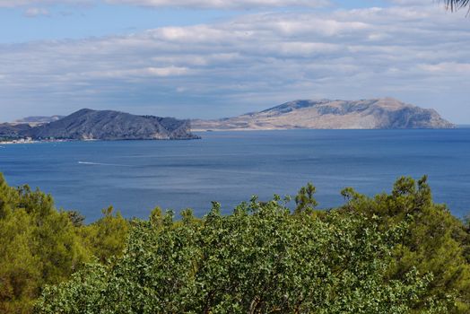 A beautiful landscape of the sea water with a boat sailing in the distance leaving behind a long raging trail among the water surface against the backdrop of high cliffs visible in the distance.