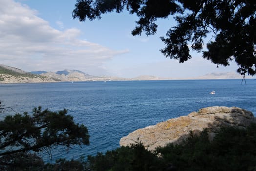 A beautiful view of the surface of the sea bay with a man on a catamaran floating near the shore and the coastline below the rocks that is seen far away.