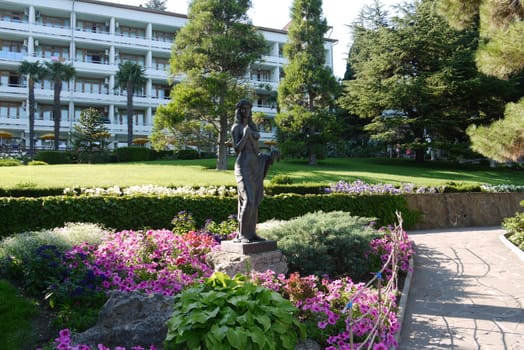 A bronze statue depicting the silhouette of a girl near a flower bed with flowers against the backdrop of a hotel complex