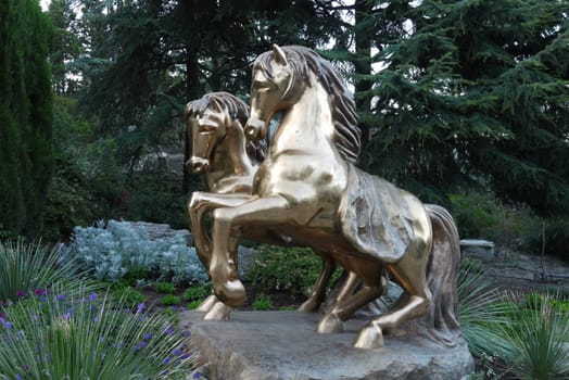 A pedestal depicting two golden smooth horses, against a background of a green park zone