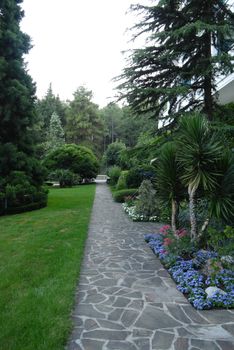 An even and beautiful path along the building of the sanatorium is laid out from various forms of stones with growing flowerbeds with flowers and a green lawn.