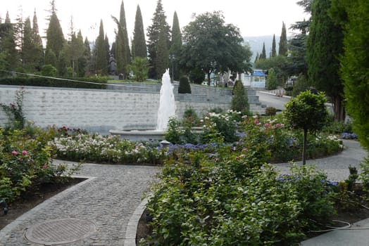 Fountain surrounded by decorative flower beds in the background of a park walking area