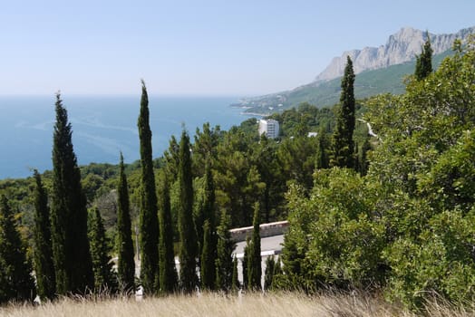 A high residential building is surrounded by dense trees on the background of high mountains