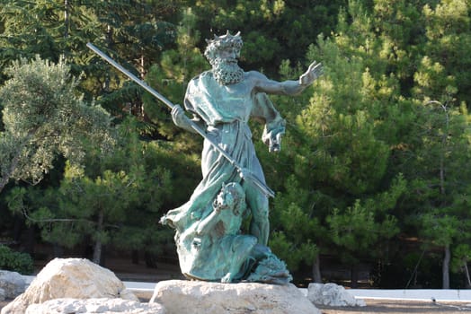 Sculpture of Neptune with a spear on a stone in the background of a coniferous park