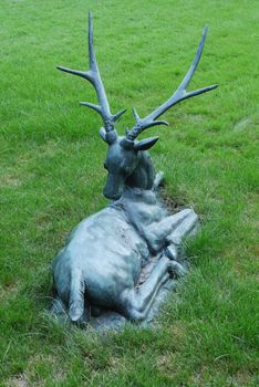 A tin statue of a deer with large branched horns on a green lawn