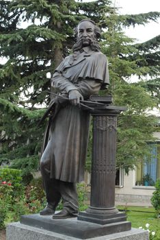 a black monument to an artist with brushes in his hands in a park near a fir and a larch