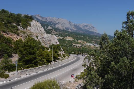 the road is twisted in the middle of the great mountains covered with trees on the background of a blue sky