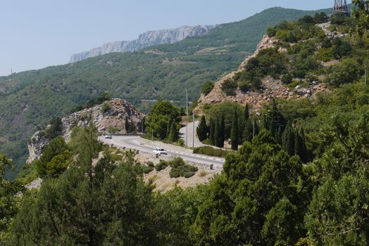 the rocky road is rolled up against the background of high mountains covered with trees