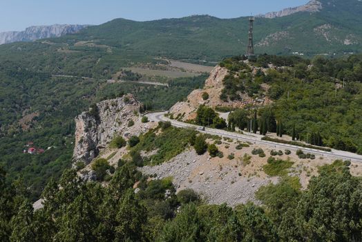 twisted rocky road against the background of high mountains covered with trees