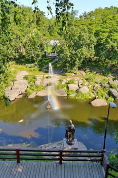 beautiful fountain in the middle of a wide rocky river on the background of dense green trees