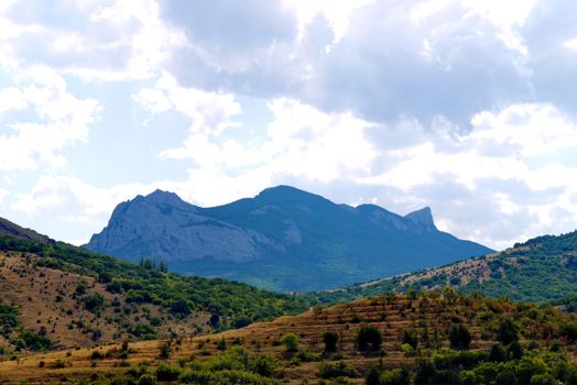 wide slopes are covered with grass under a blue cloudy sky on the background of a high rock