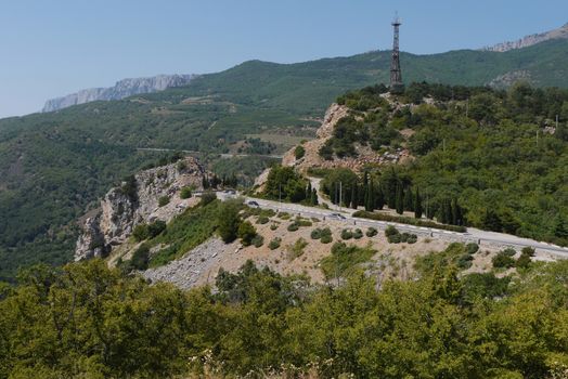 the rocky road is rolled up against the background of high mountains covered with trees