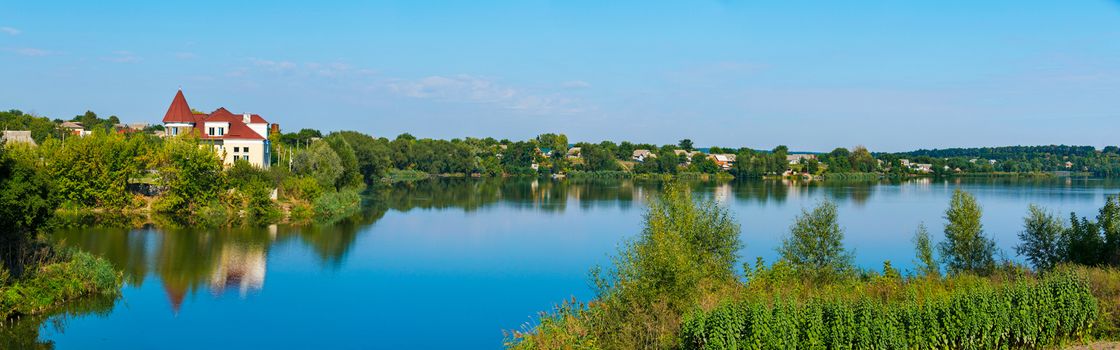 a small settlement under a blue sky on the shores of a wide deep lake