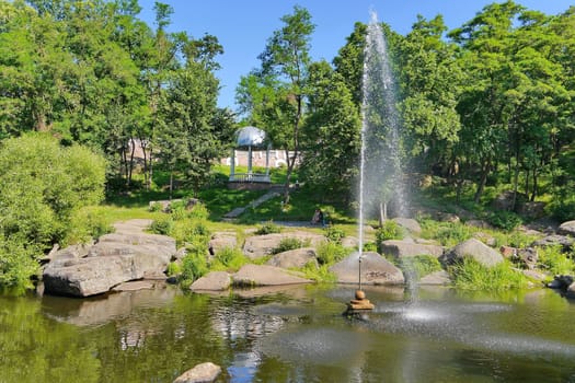 beautiful fountain in the middle of a wide rocky river on the background of dense green trees