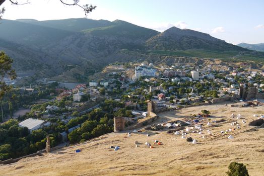 a small cozy town surrounded by high grassy slopes on a blue sky background