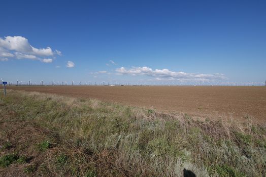 broad endless field under the blue sky on the background of high windmills