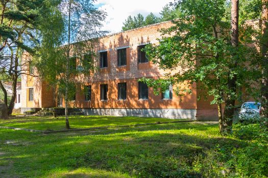 The large abandoned brick building is surrounded by tall, slender trees