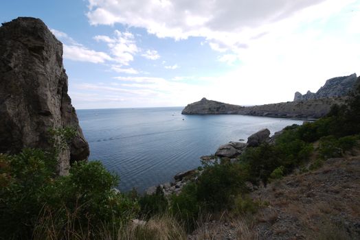 The wide bay is surrounded by high Crimean rocks covered with grass