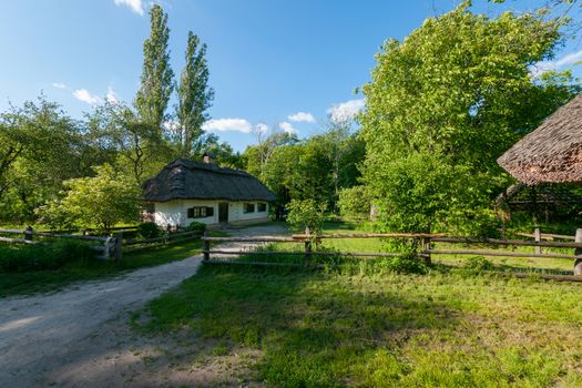 The Ukrainian village house is fenced with a fence of twigs among the green trees