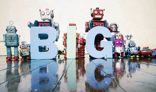 the word BIG held by old robot toys on wooden floor