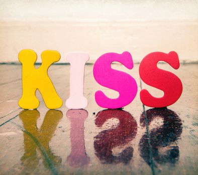 the word Kiss with color wooden letters on a wooden floor with reflection 