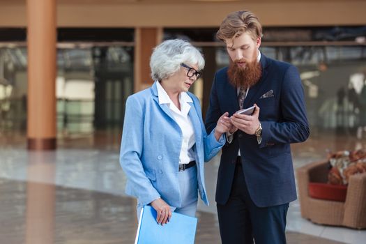 Young business man and senior woman look together at mobile phone