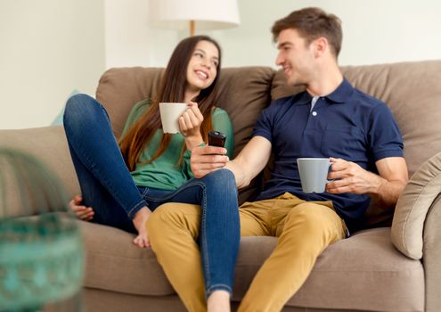 Young couple on the sofa drinking coffee while watching tv