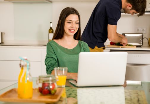 Man cooking while her wife working on a laptop