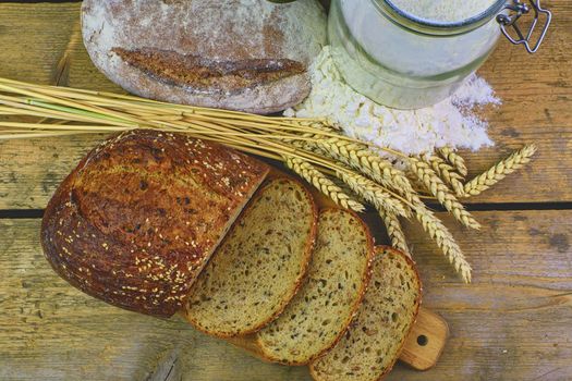 Loafs of bread, slices of bread, wheat flour and ears of grain on wood background. Rustic and rural concept. Close up. Flat lay. 