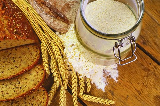 Loafs of bread, slices of bread, wheat flour and ears of grain on wood background. Rustic and rural concept. Close up. Flat lay. 