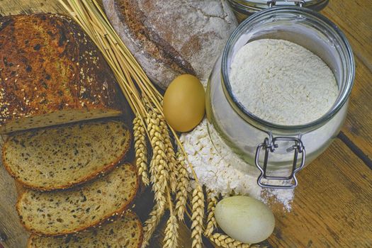 Loafs of bread, slices of bread, wheat flour, eggs and ears of grain on wood background. Rustic and rural concept. Close up. Flat lay.  