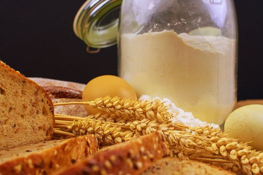 Loafs of bread, slices of bread, wheat flour, eggs and ears of grain on wood background. Rustic and rural concept. Close up. Copy space.