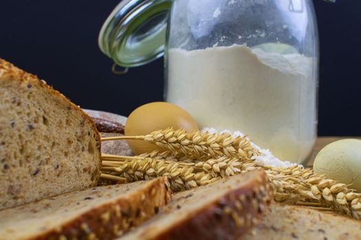 Loafs of bread, slices of bread, wheat flour, eggs and ears of grain on wood background. Rustic and rural concept. Close up. Copy space.